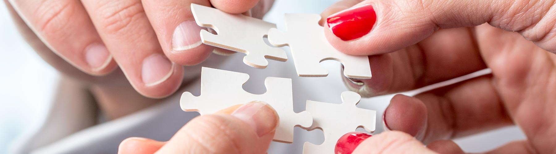 four people each holding a large puzzle piece towards each other